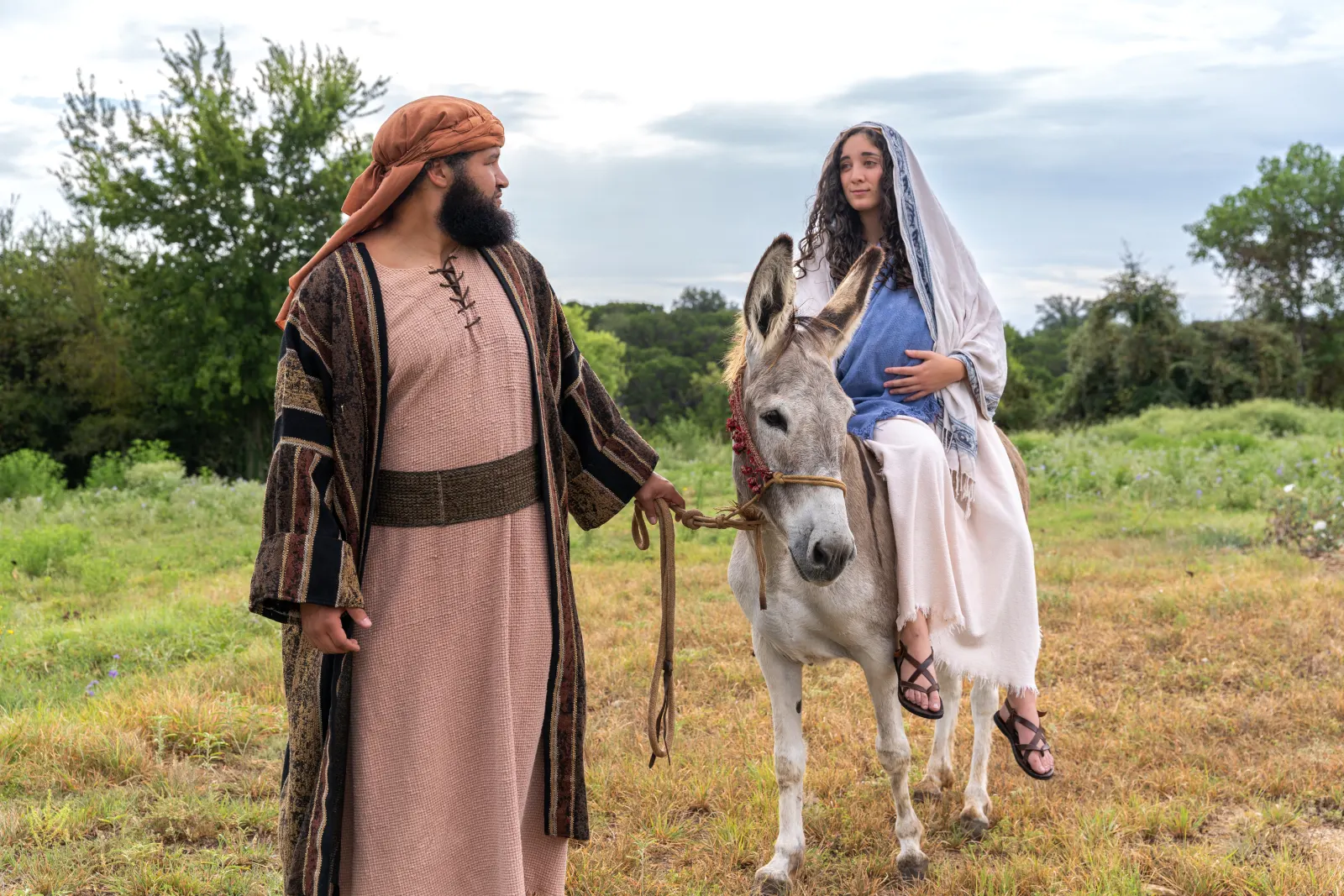 Costumed travelers guide a woman riding a donkey through an open field during a biblical production.