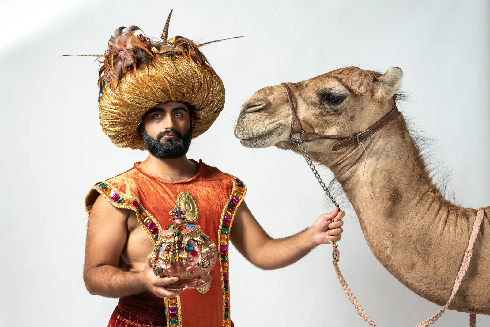 Costumed handler stands beside a camel during a studio photography session.